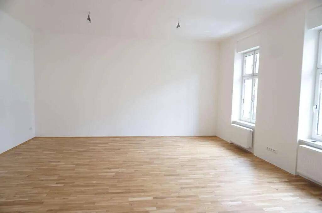 Geräumiger, heller Raum mit Holzboden und zwei Fenstern, bereit zur individuellen Gestaltung.