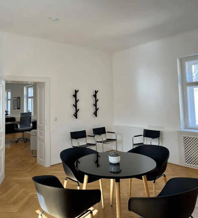 Heller Wartebereich mit modernem runden Tisch, schwarzen Stühlen und dekorativen Wandhaken.