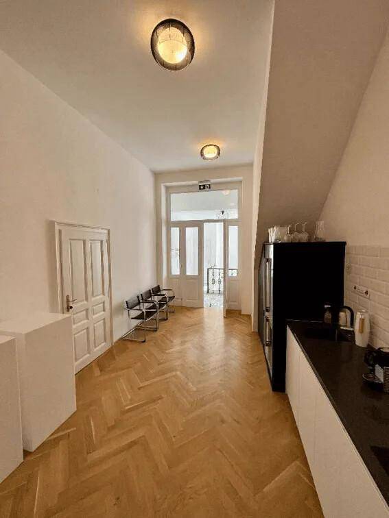 Langer Flur mit Fischgrätparkett, einer kleinen Küchenzeile und Blick zum Eingangsbereich.