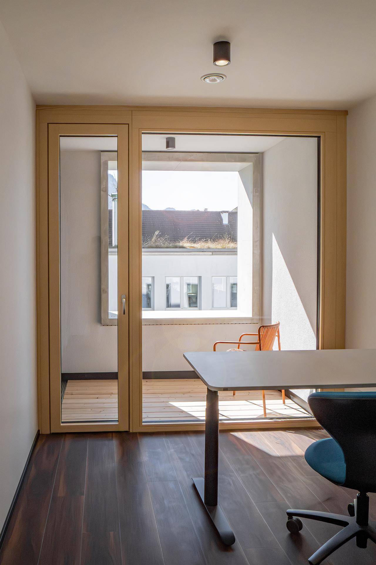 Heller Raum mit Holzboden, Schreibtisch und Zugang zu einem Balkon.