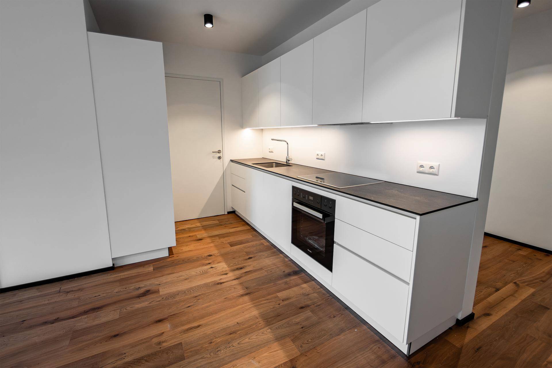 Moderne Einbauküche mit weißen Schränken, dunkler Arbeitsplatte und integriertem Backofen.