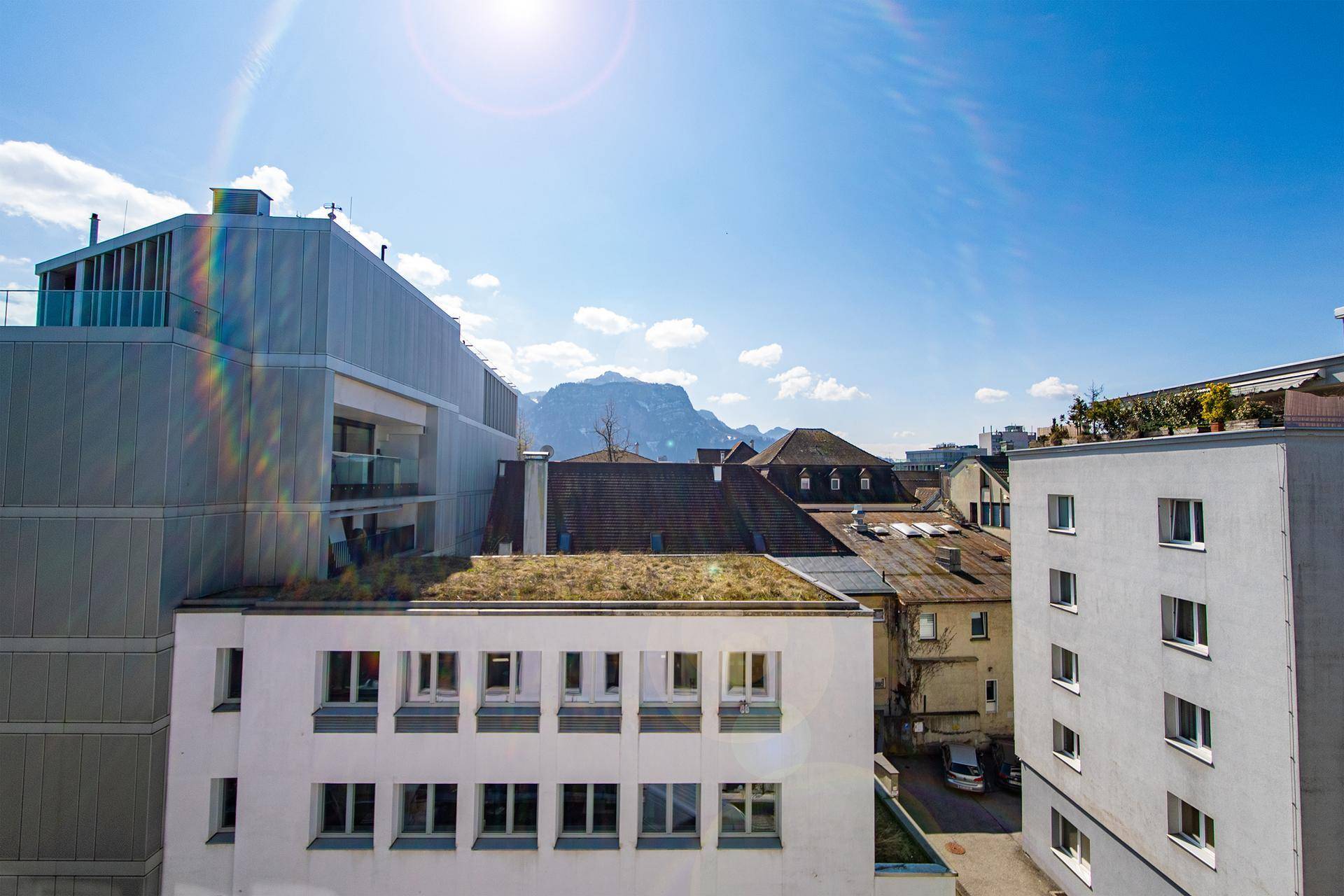 Panoramablick über die Dächer der Stadt mit majestätischen Bergen im Hintergrund unter blauem Himmel.