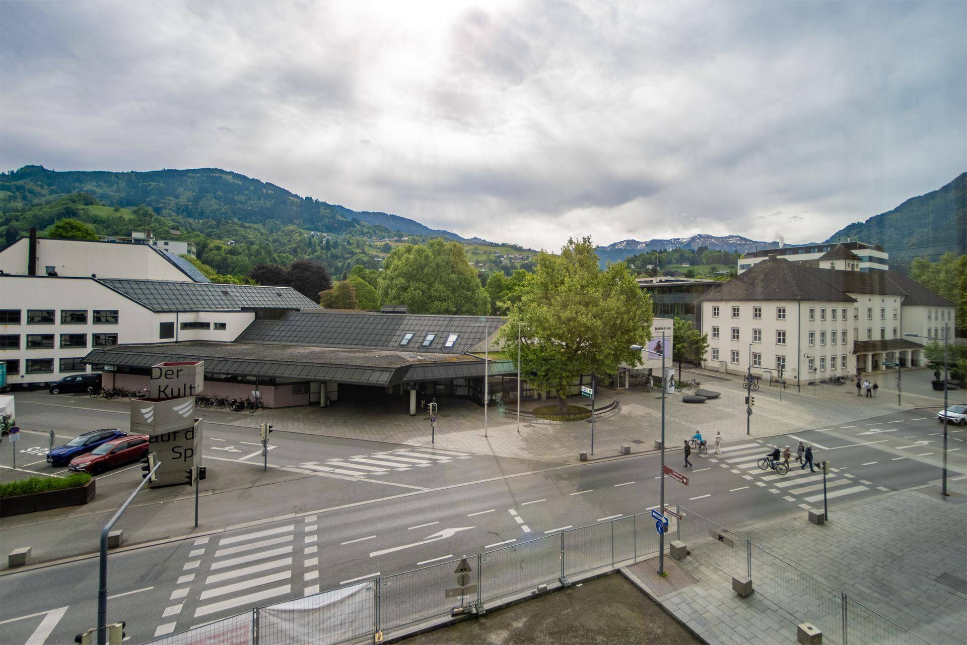 Weitblick über eine Stadt mit Bergen im Hintergrund, gesehen durch ein Fenster.