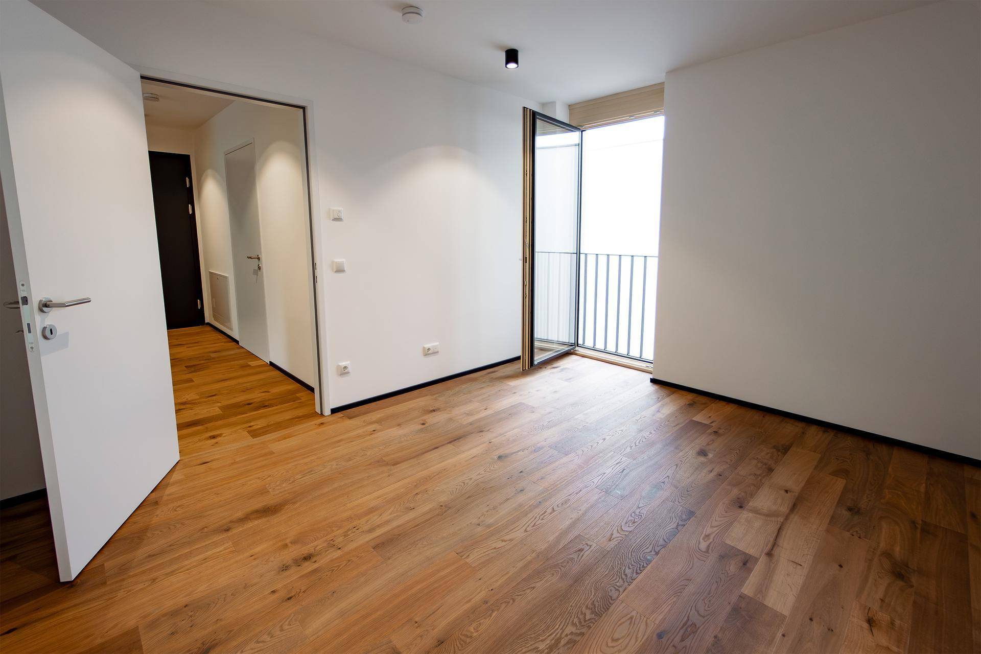 Helles Schlafzimmer mit Holzboden und einem französischen Balkon, bereit zur individuellen Gestaltung.