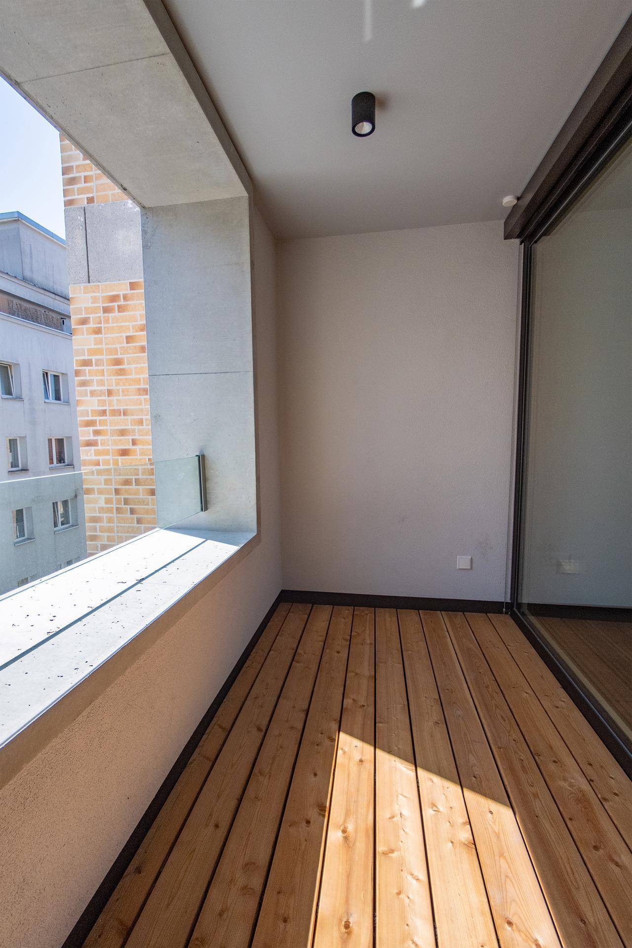 Sonniger Balkon mit Holzboden und Blick auf die umliegenden Gebäude.