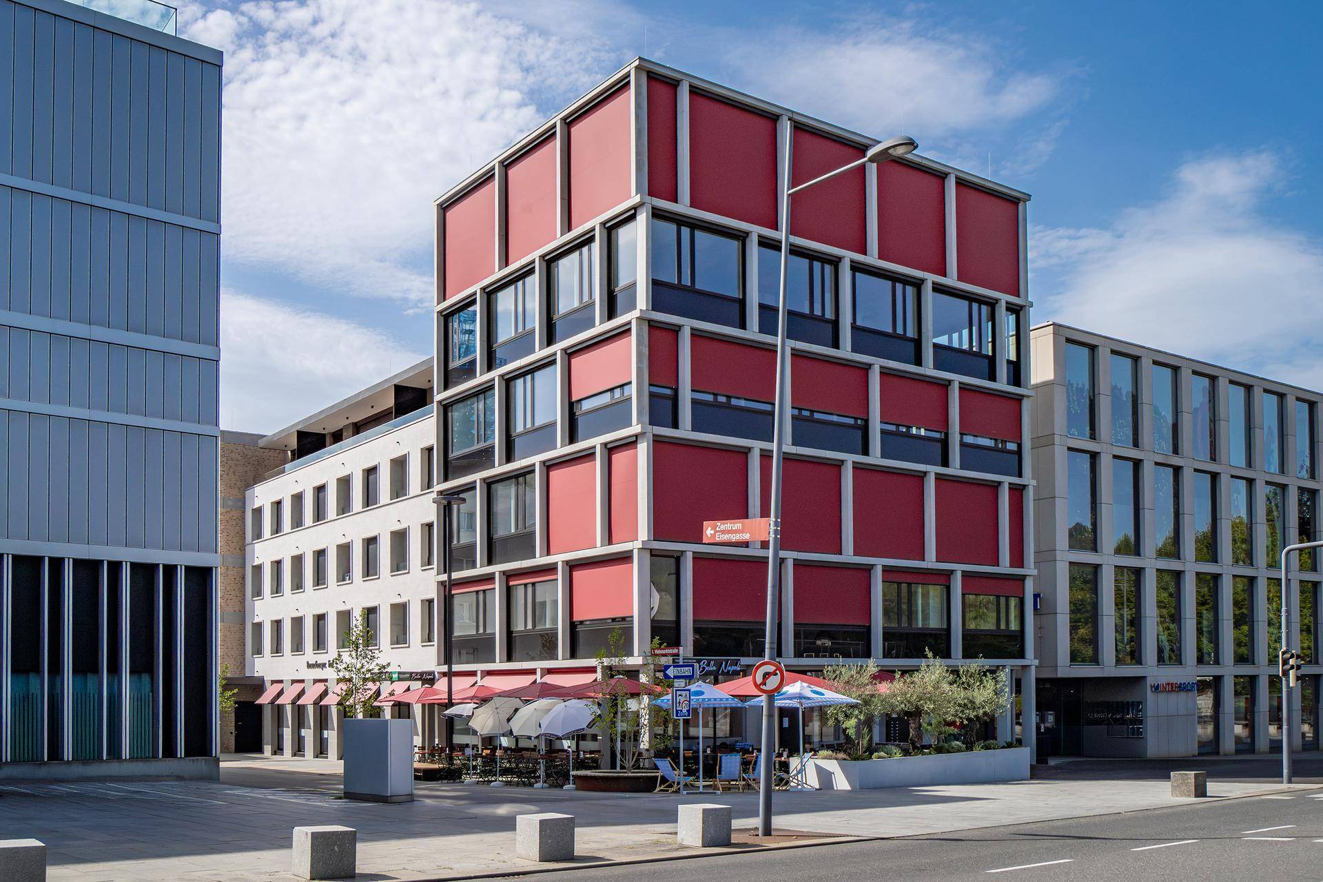 Ansicht eines modernen Gebäudes mit roten Fensterläden und umliegender Stadtlandschaft.