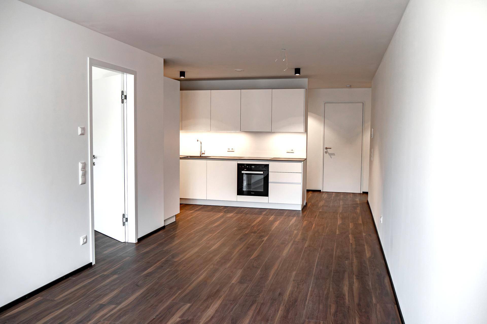 Offene Küche mit weißen Schränken, integriertem Backofen und dunklem Holzboden.