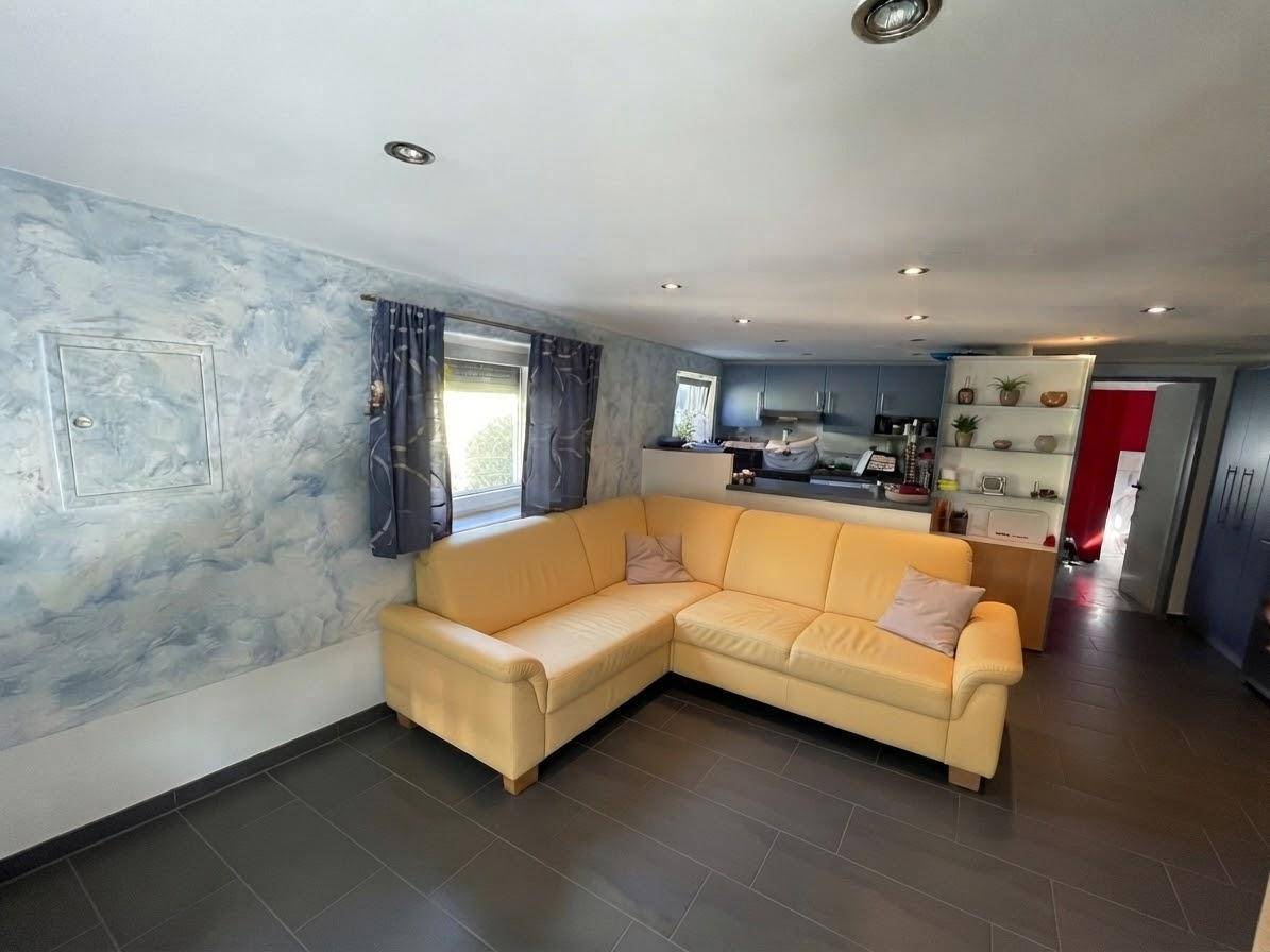 Gemütliches Wohnzimmer mit gelbem Ecksofa, blauer Wandgestaltung und offener Verbindung zur Küche.