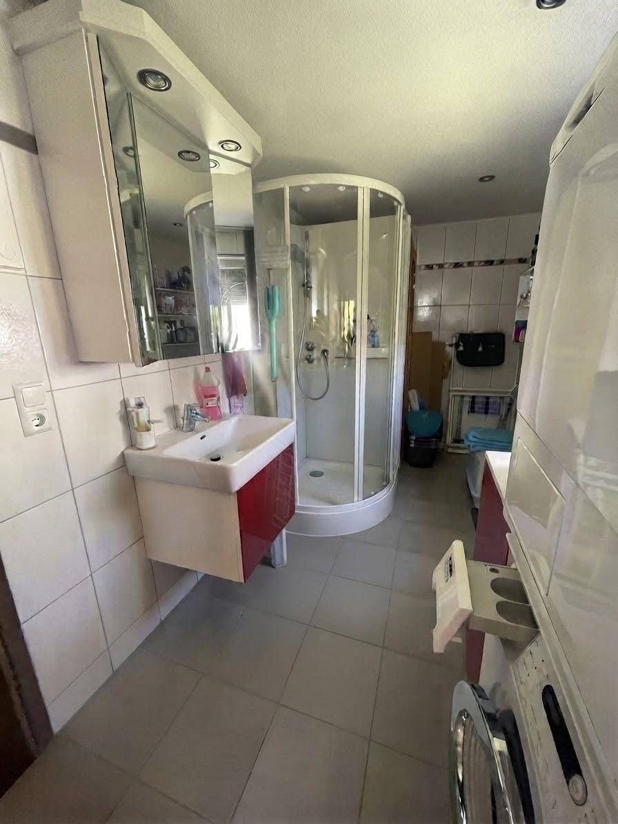 Badezimmer mit Duschkabine, Waschbecken und Waschmaschine, hell gefliest.