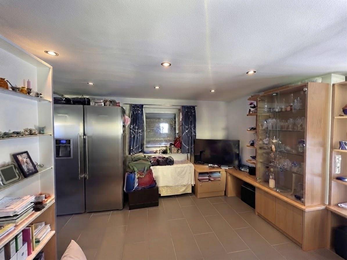 Geräumiger Wohnbereich mit Fliesenboden, Regalen und einem großen Kühlschrank.