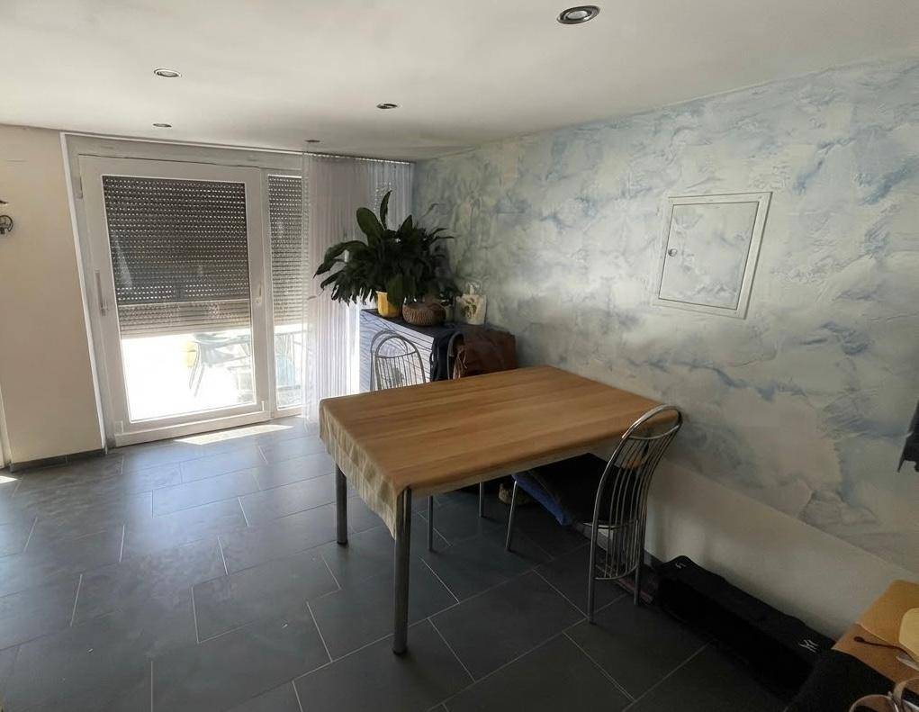 Essbereich mit Holztisch, Fliesenboden und Zugang zu einer Terrasse durch eine große Tür.