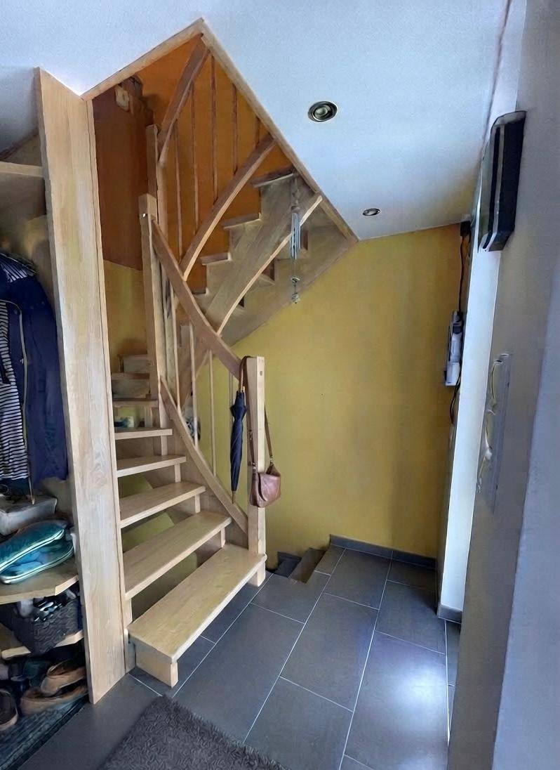 Heller Flur mit Holztreppe, gelber Wand und praktischem Stauraum unter der Treppe.