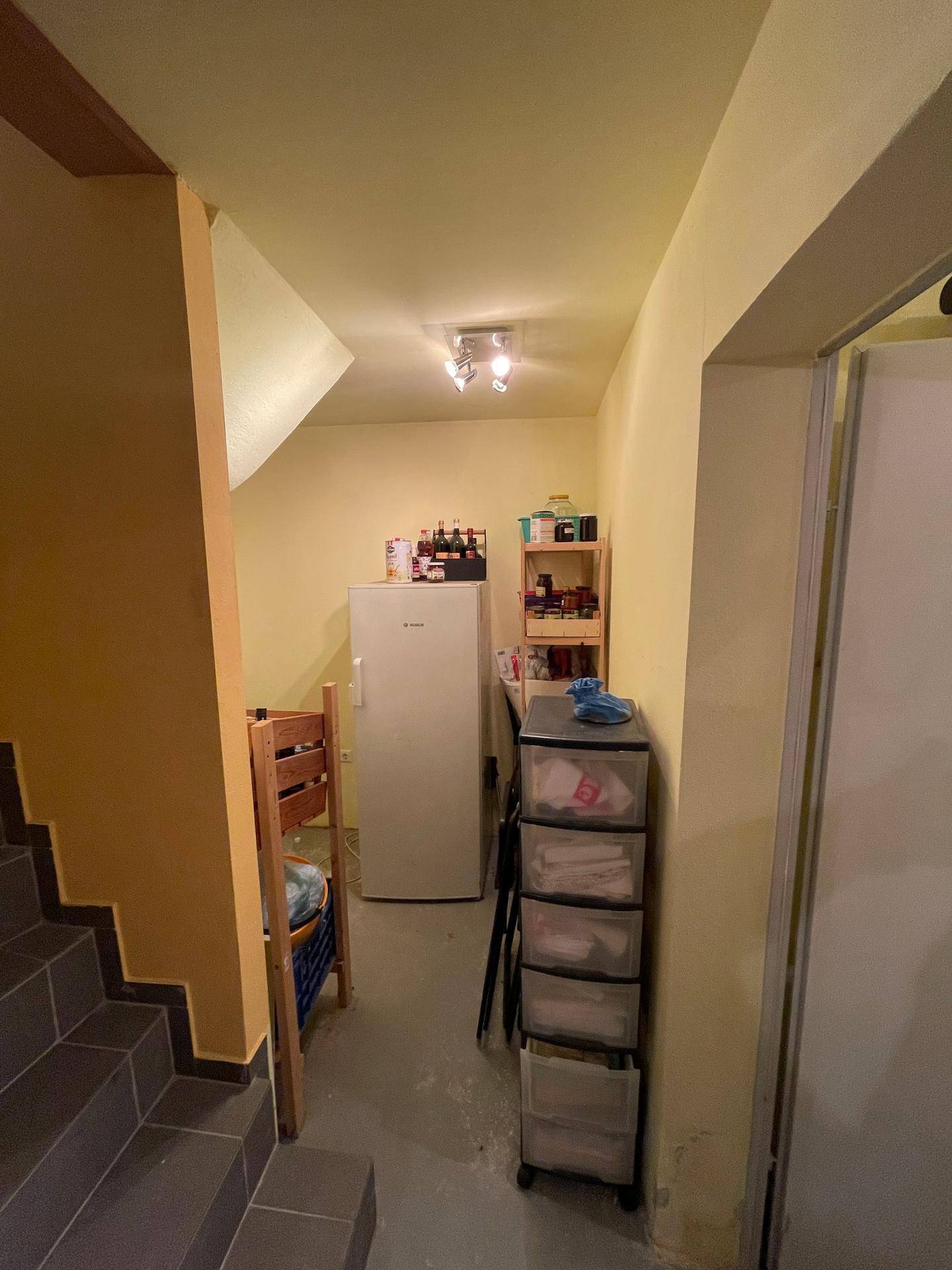 Kellerraum mit Fliesenboden, Kühlschrank und Regalen, ideal als Abstellfläche.