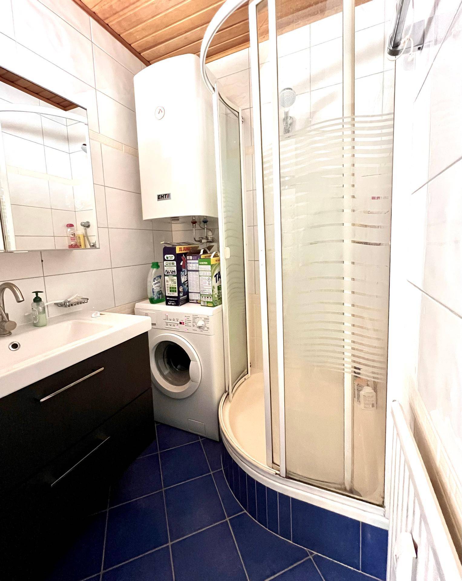 Badezimmer mit Duschkabine, Waschbecken und blauen Bodenfliesen.