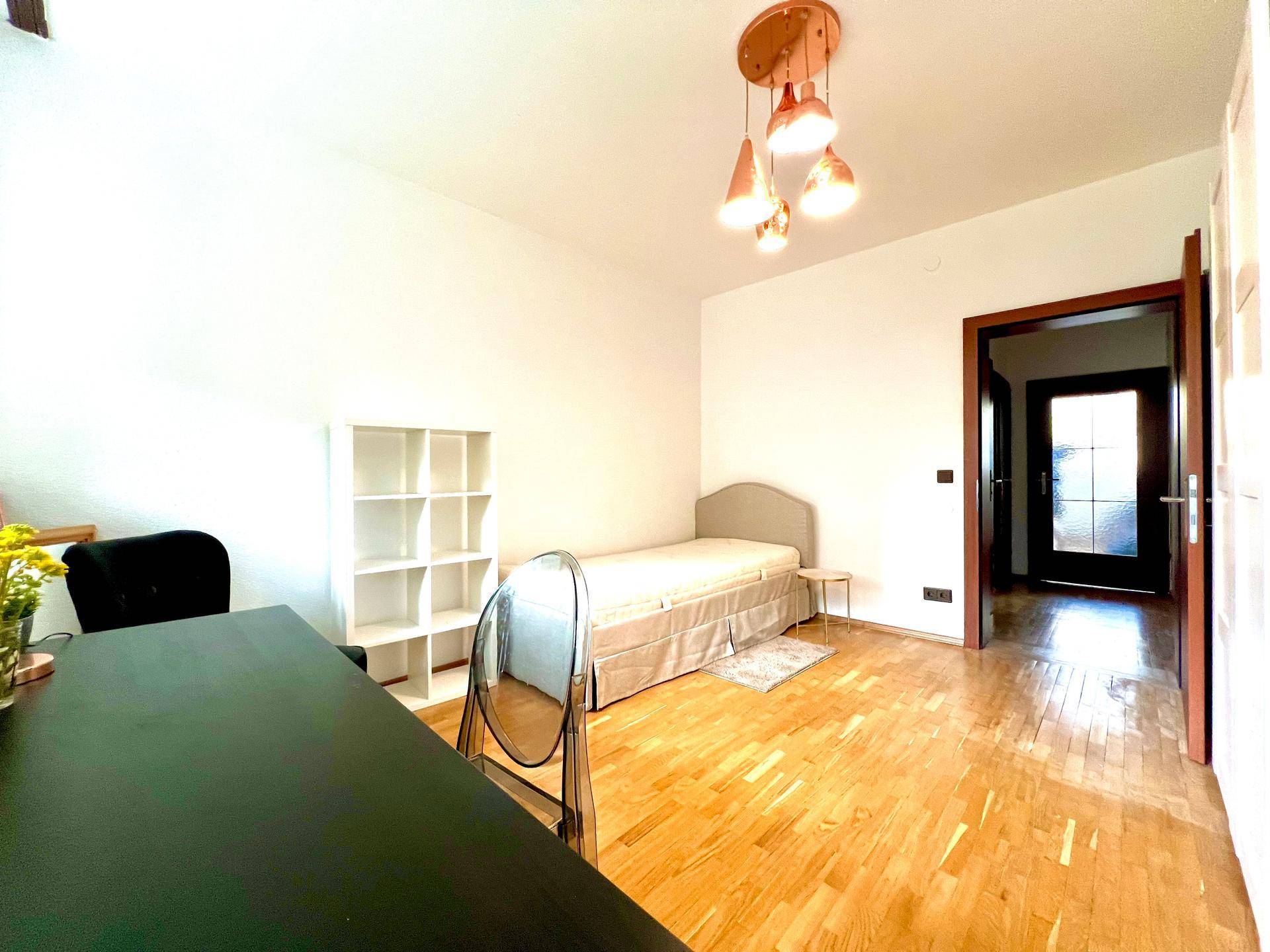 Freundliches Schlafzimmer mit Holzboden, Schreibtisch und Regalsystem.