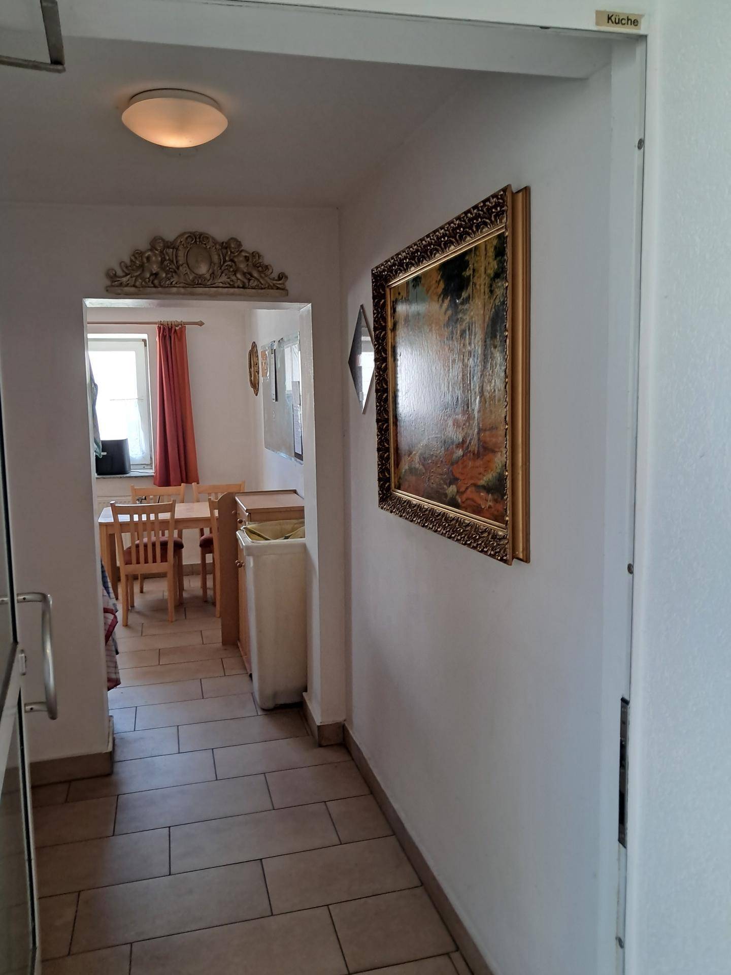 Flur mit Fliesenboden und Blick in einen angrenzenden Essbereich mit Fenster.