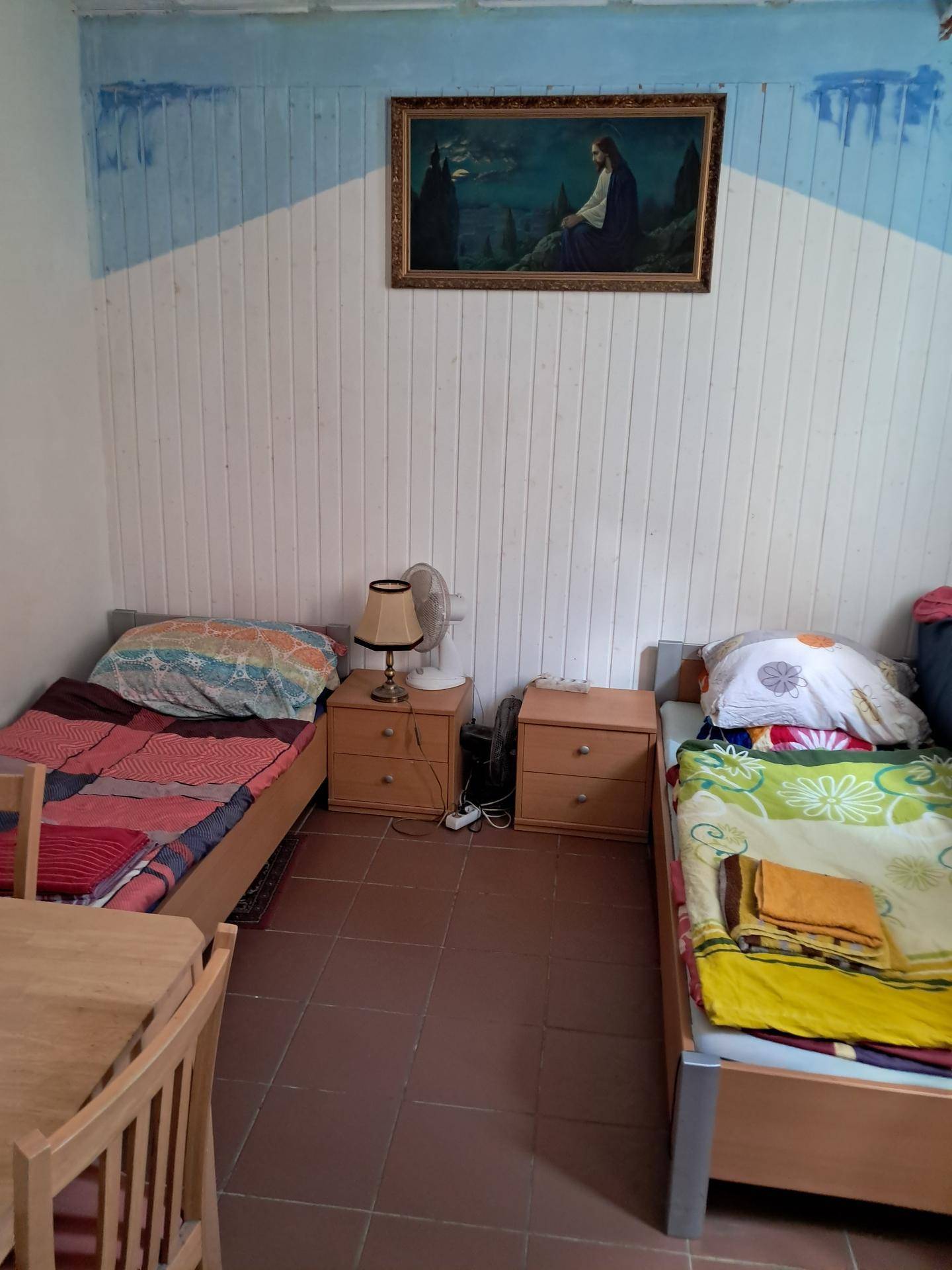 Schlafzimmer mit zwei Einzelbetten, Terrakotta-Fliesenboden und einfacher Holzvertäfelung an der Wand.