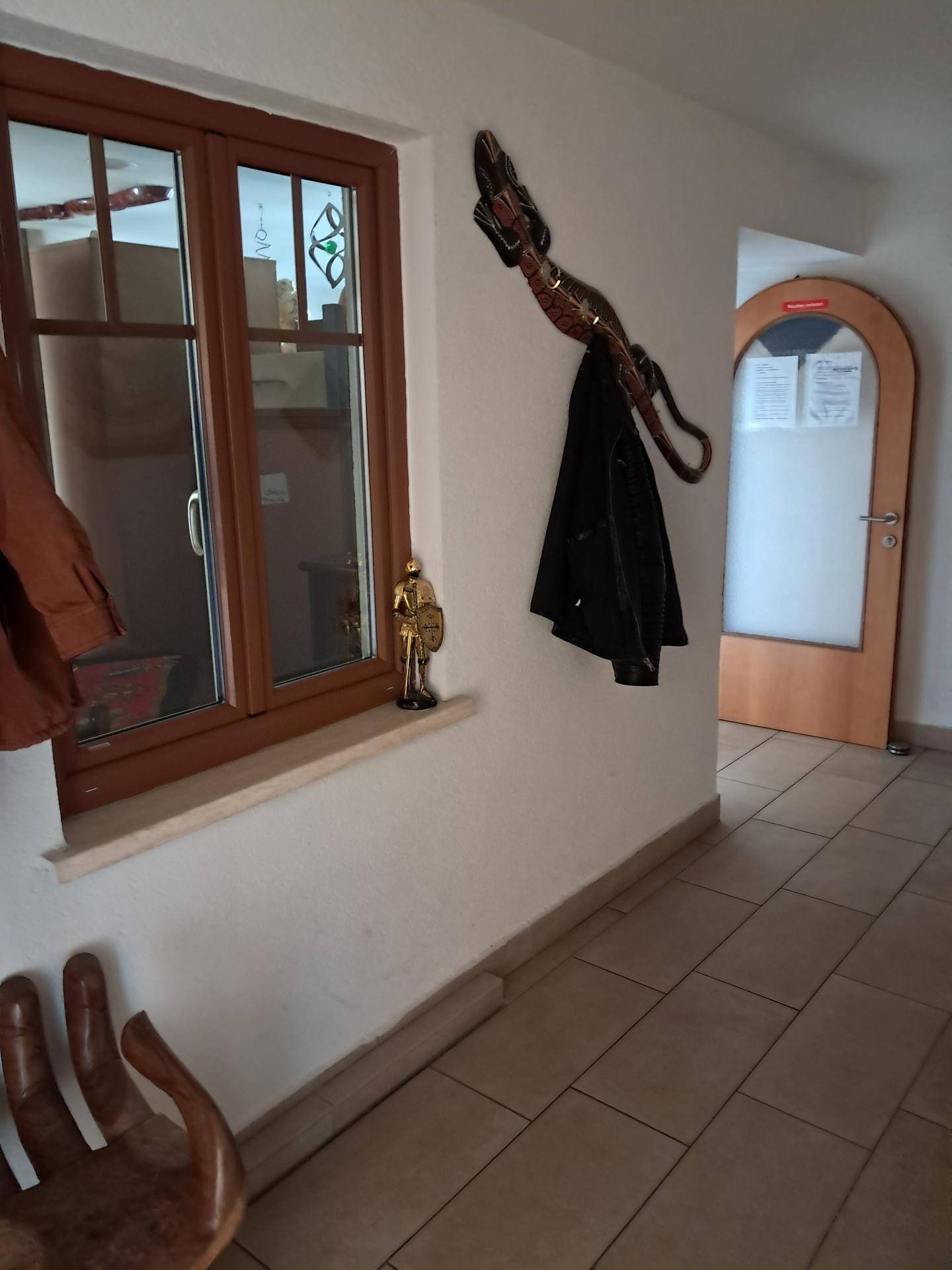 Flur mit Fenster, Garderobe und einem Holzelement, das natürliches Licht hereinlässt.