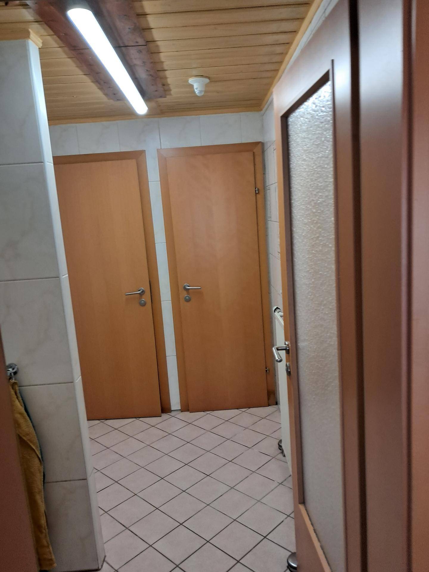 Badezimmerbereich mit gefliestem Boden und mehreren Holztüren.