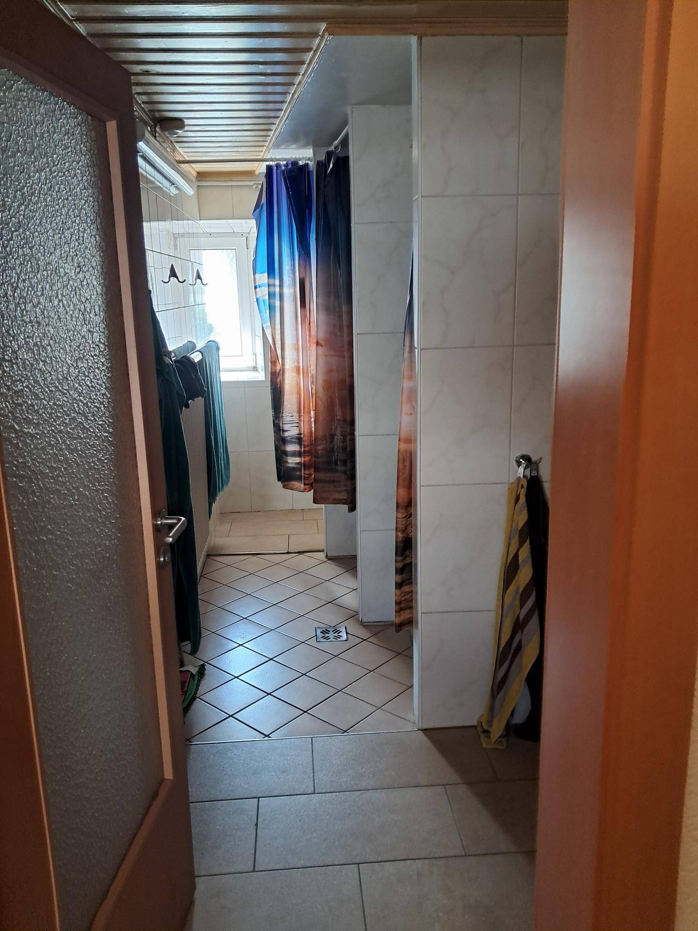 Badezimmer mit mehreren Duschkabinen, gefliesten Wänden und einem Fenster für Tageslicht.
