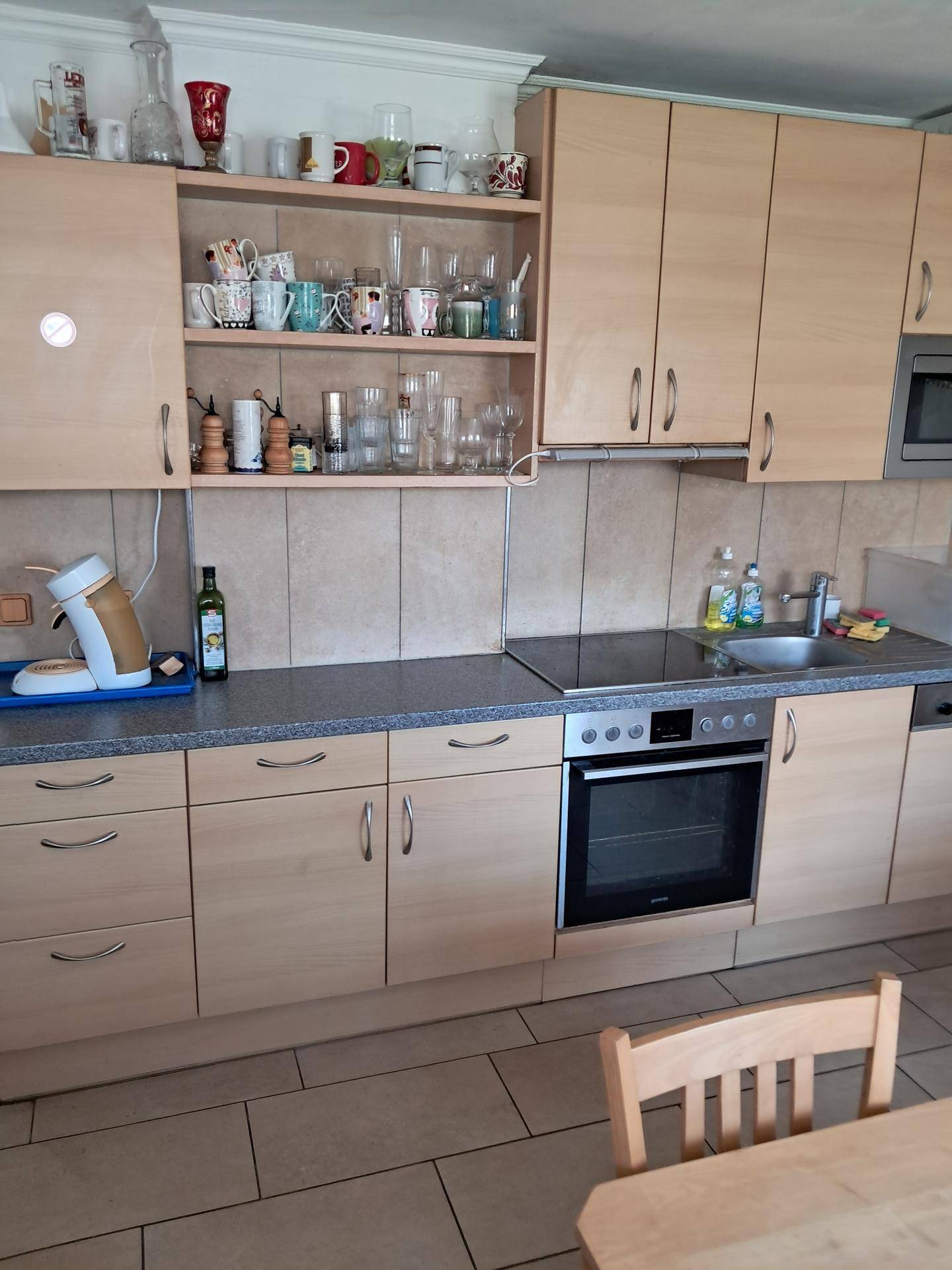 Detailansicht der Küche mit hellen Holzfronten, Kochfeld, Backofen und Spülmaschine.