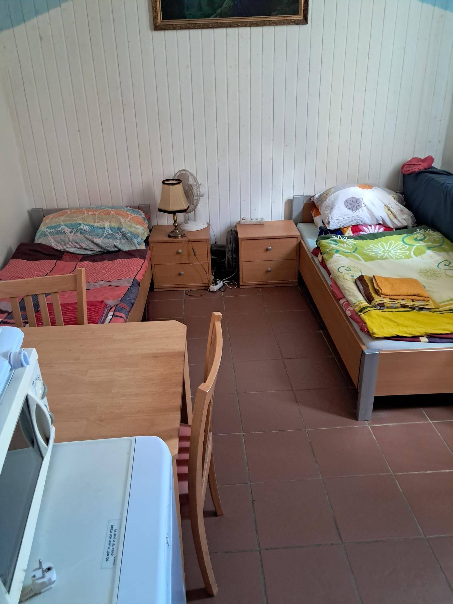 Einfaches Schlafzimmer mit zwei Einzelbetten, Nachttischen und farbenfroher Bettwäsche.