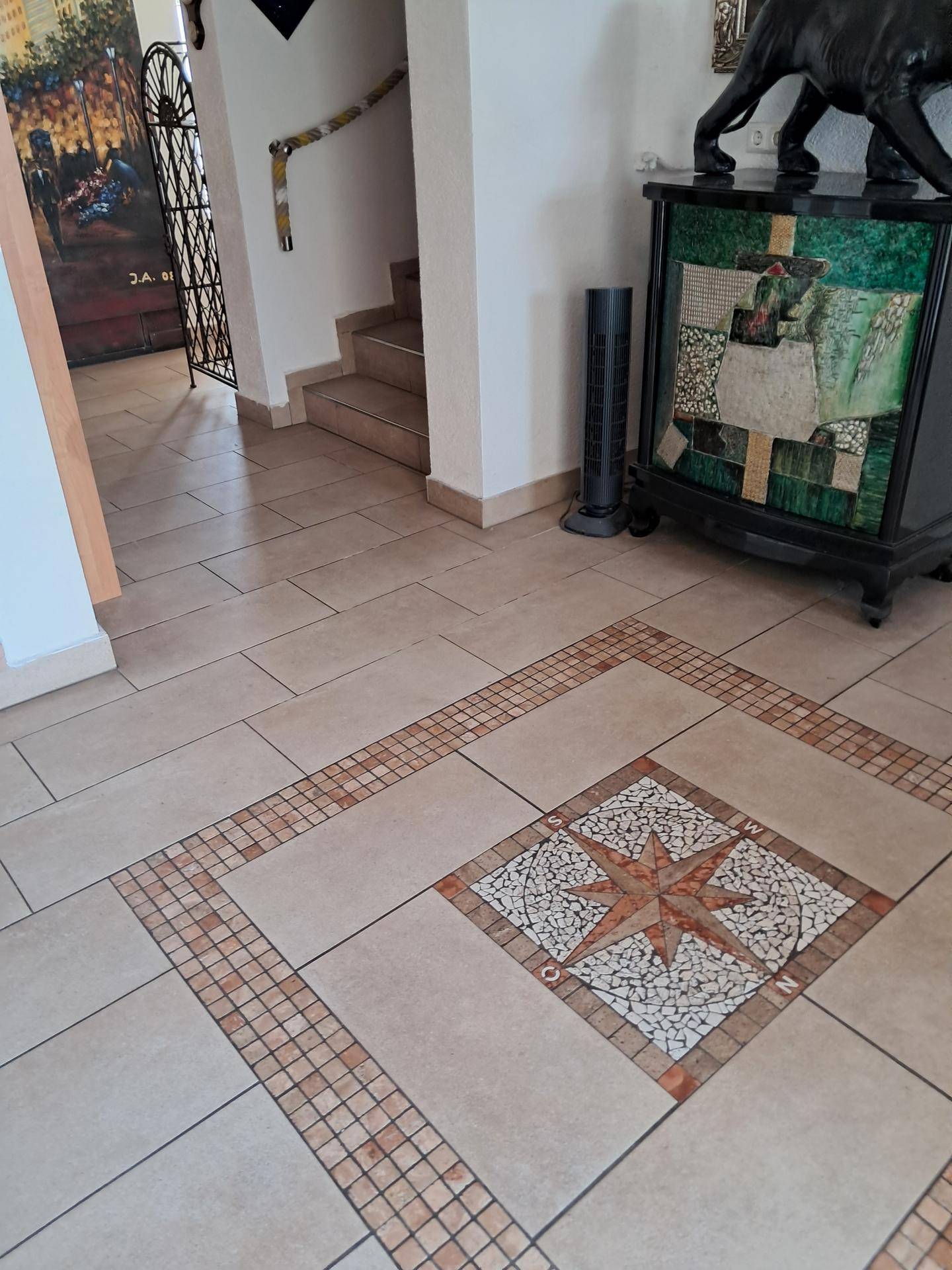 Flur mit hellem Fliesenboden, dekorativem Mosaik und einem Treppenaufgang.