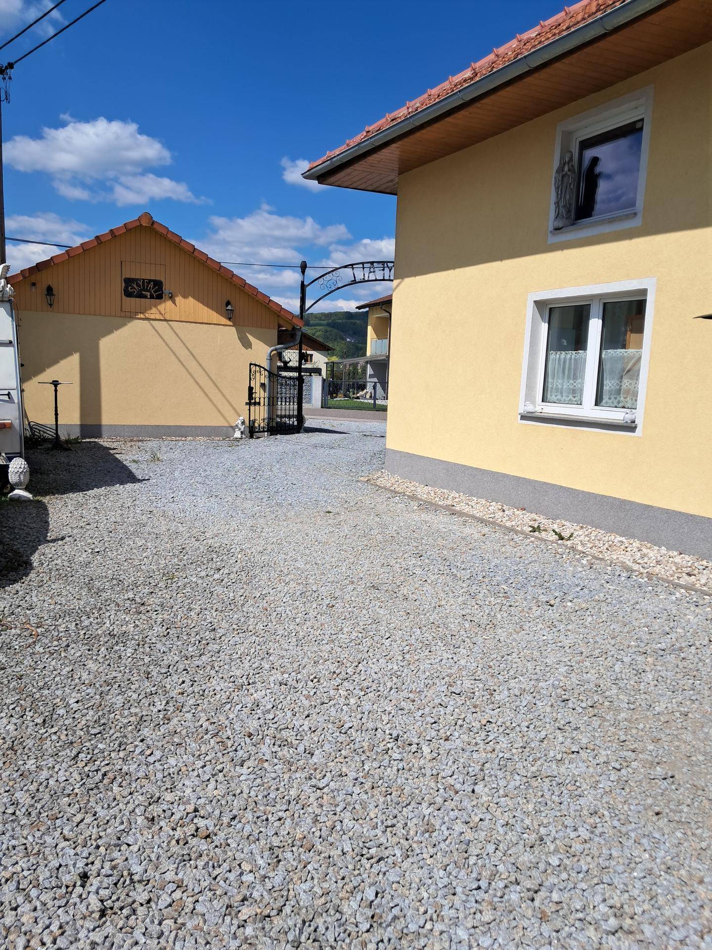 Außenansicht des Gebäudes mit gelber Fassade, Schotterauffahrt und Blick auf die ländliche Umgebung.