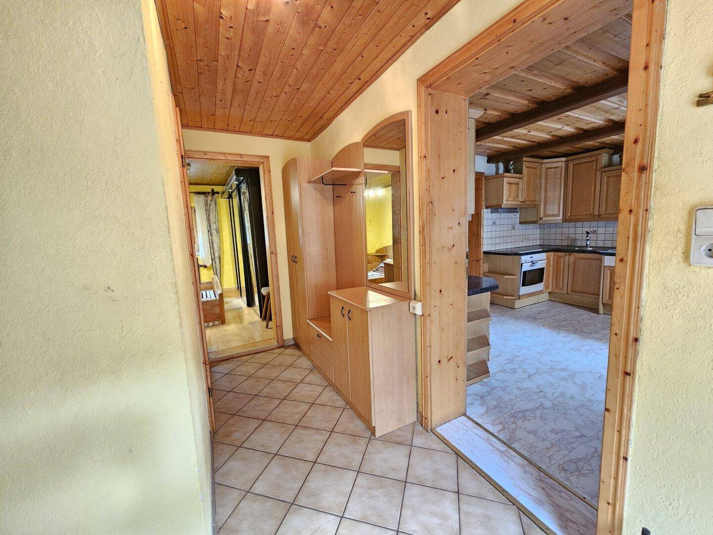 Flur mit Holzdecke, Fliesenboden und Garderobe, führt in Küche und Schlafzimmer.