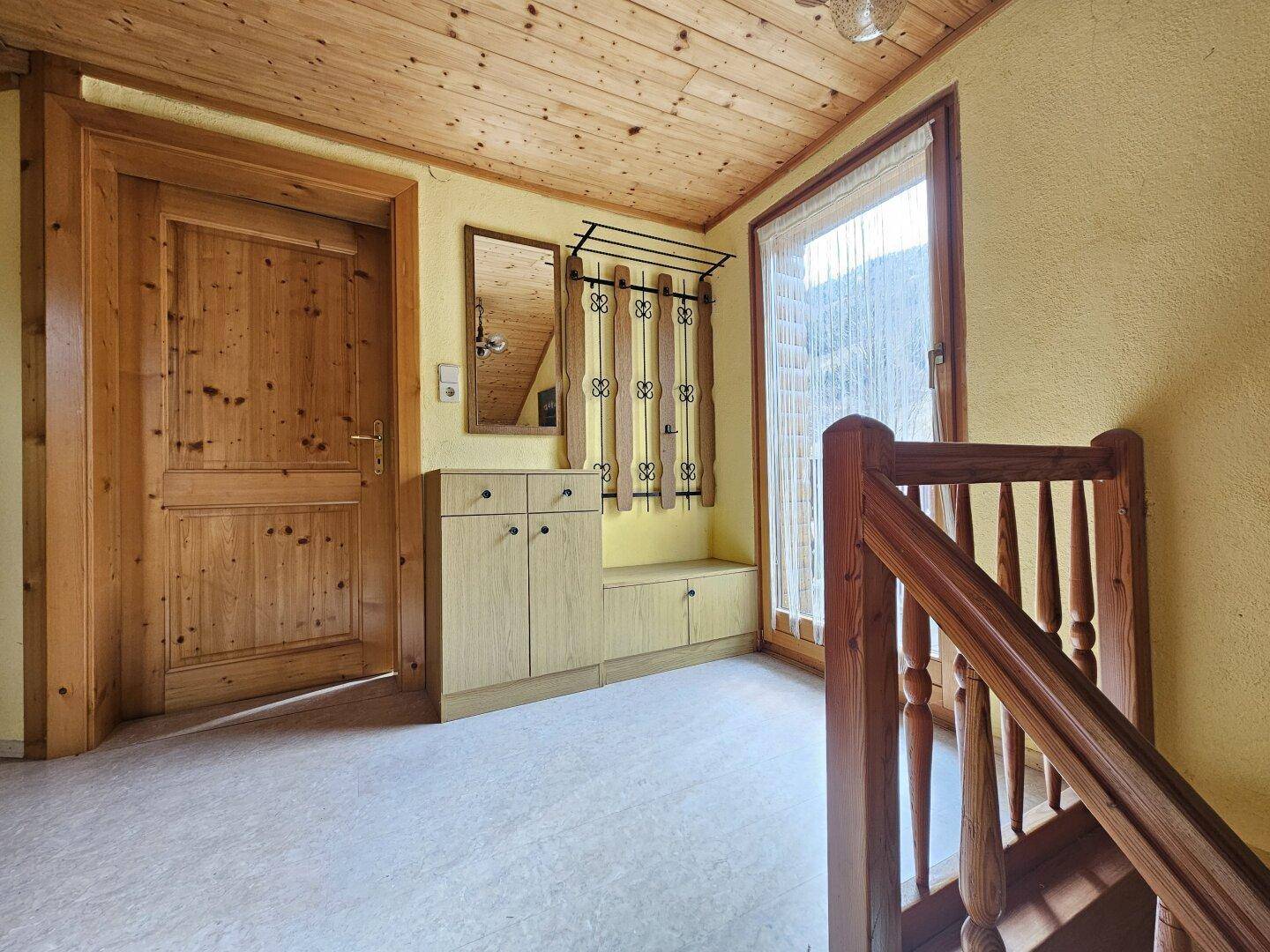 Heller Flur mit Holzdecke, Garderobe und Zugang zu einem Balkon oder Fenster.