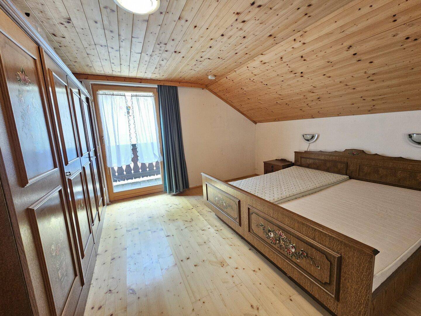 Schlafzimmer im Dachgeschoss mit Holzdecke, Holzboden und Zugang zum Balkon.