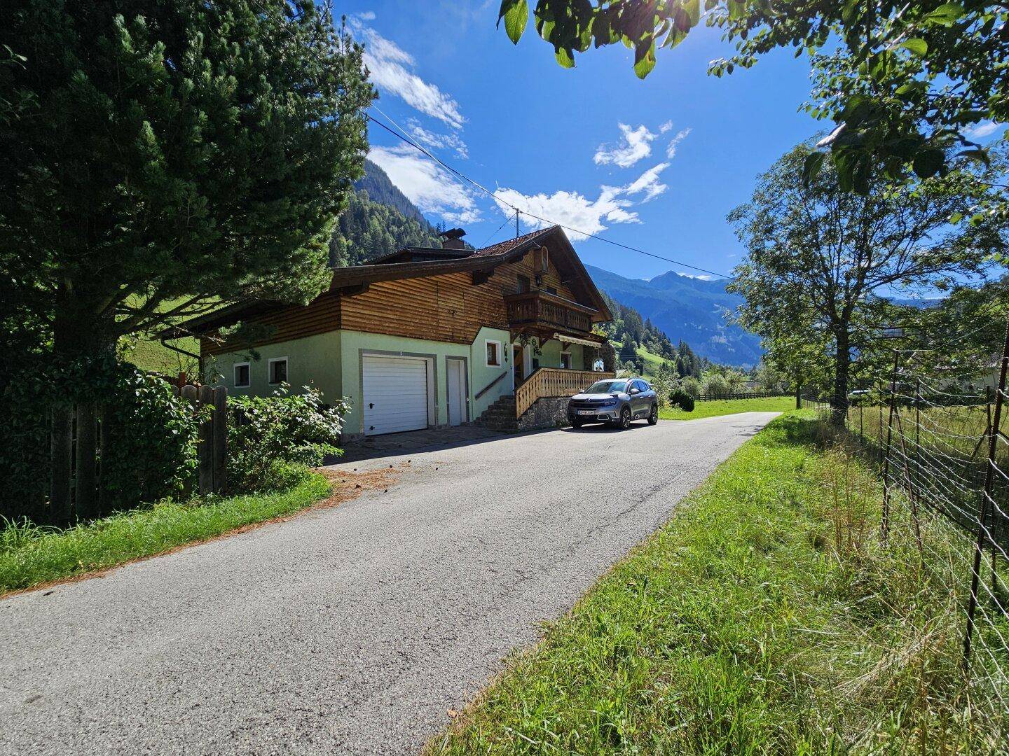 Haus in ländlicher Umgebung mit Garage und Zufahrt, umgeben von Bergen.