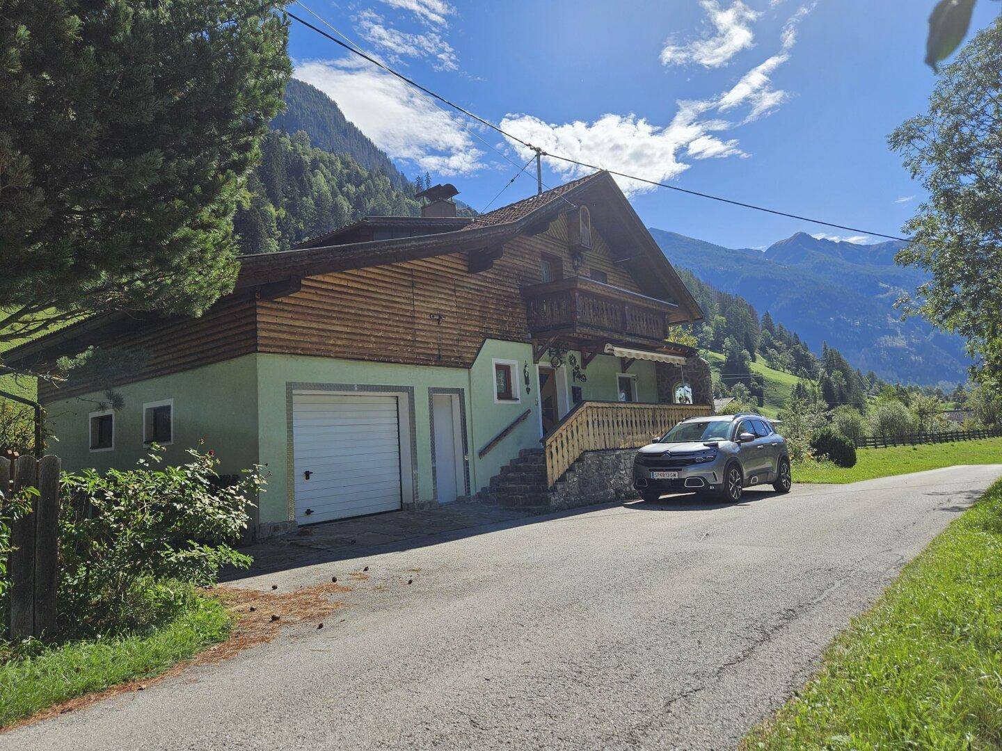 Traditionelles Haus mit Holzverkleidung und Garage, eingebettet in eine Berglandschaft.