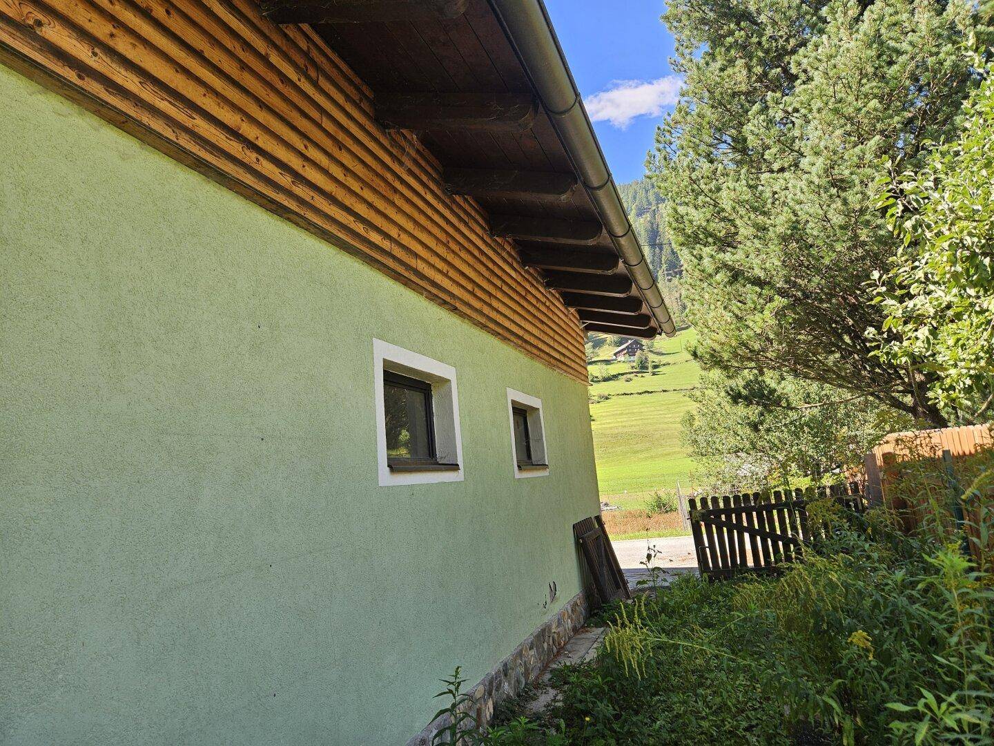 Seitenansicht des Hauses mit kleinen Fenstern und Holzverkleidung unter dem Dach.