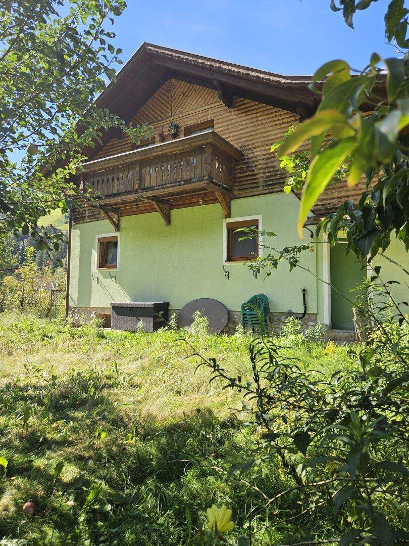 Haus von der Gartenseite aus gesehen, umgeben von üppigem Grün und Bäumen.