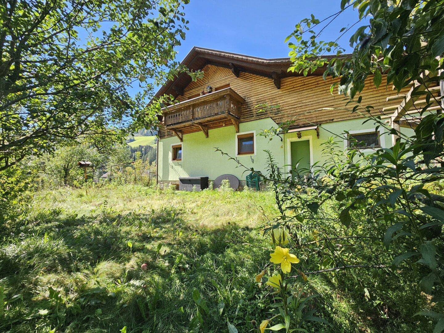 Hausansicht vom Garten aus mit blühenden Pflanzen und natürlicher Umgebung.