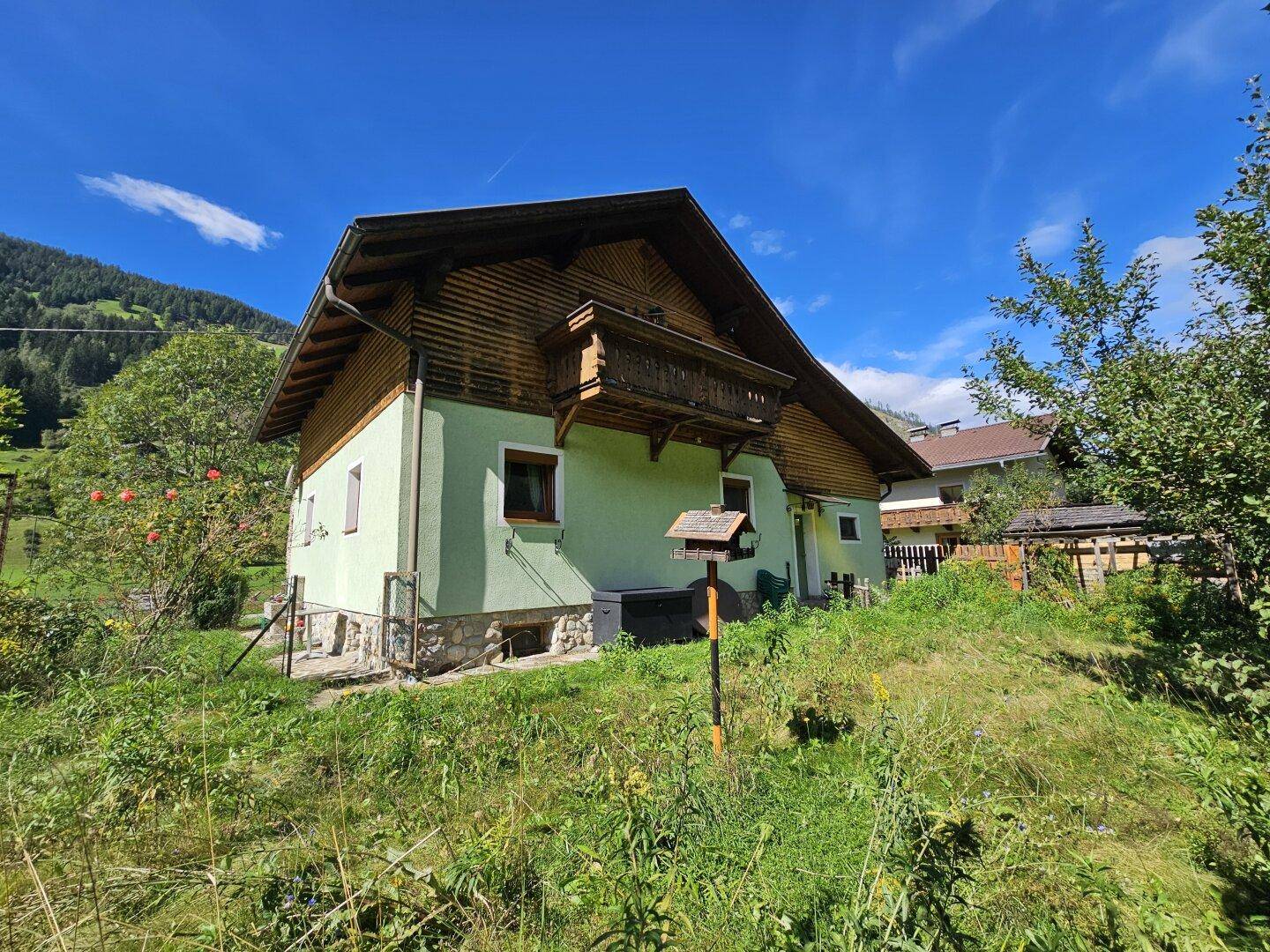 Haus mit Balkon und Garten, eingebettet in die grüne Landschaft mit Bergblick.
