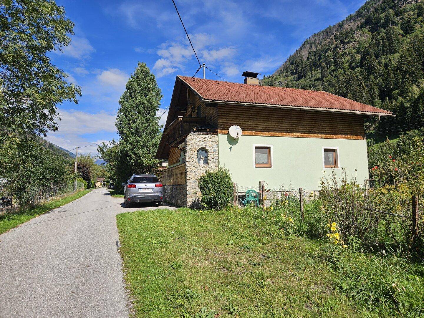 Haus in ländlicher Umgebung mit geparktem Auto und Blick auf die Berge.