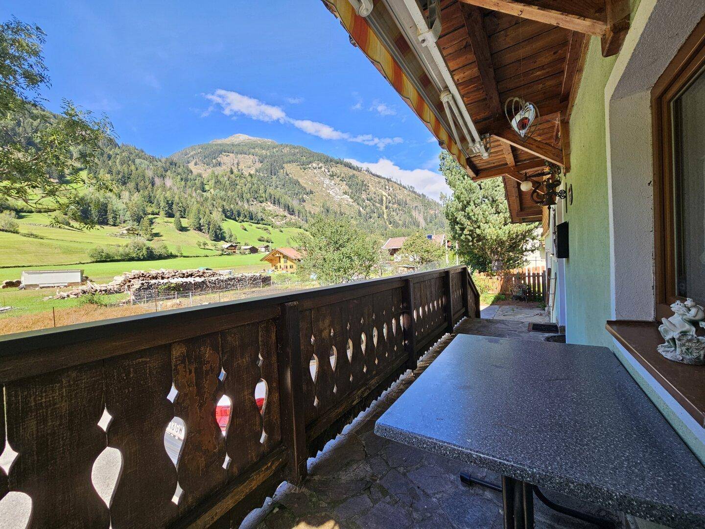 Gemütlicher Balkon mit Steintisch und weitem Blick auf die grüne Berglandschaft.