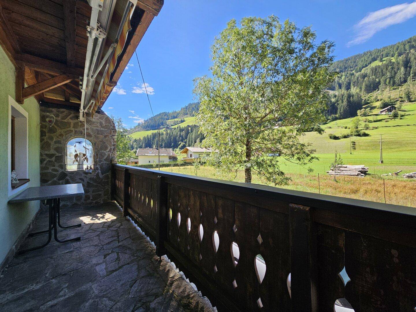 Balkon mit Holzbalkongeländer und Panoramablick auf die umliegenden Berge und Wiesen.