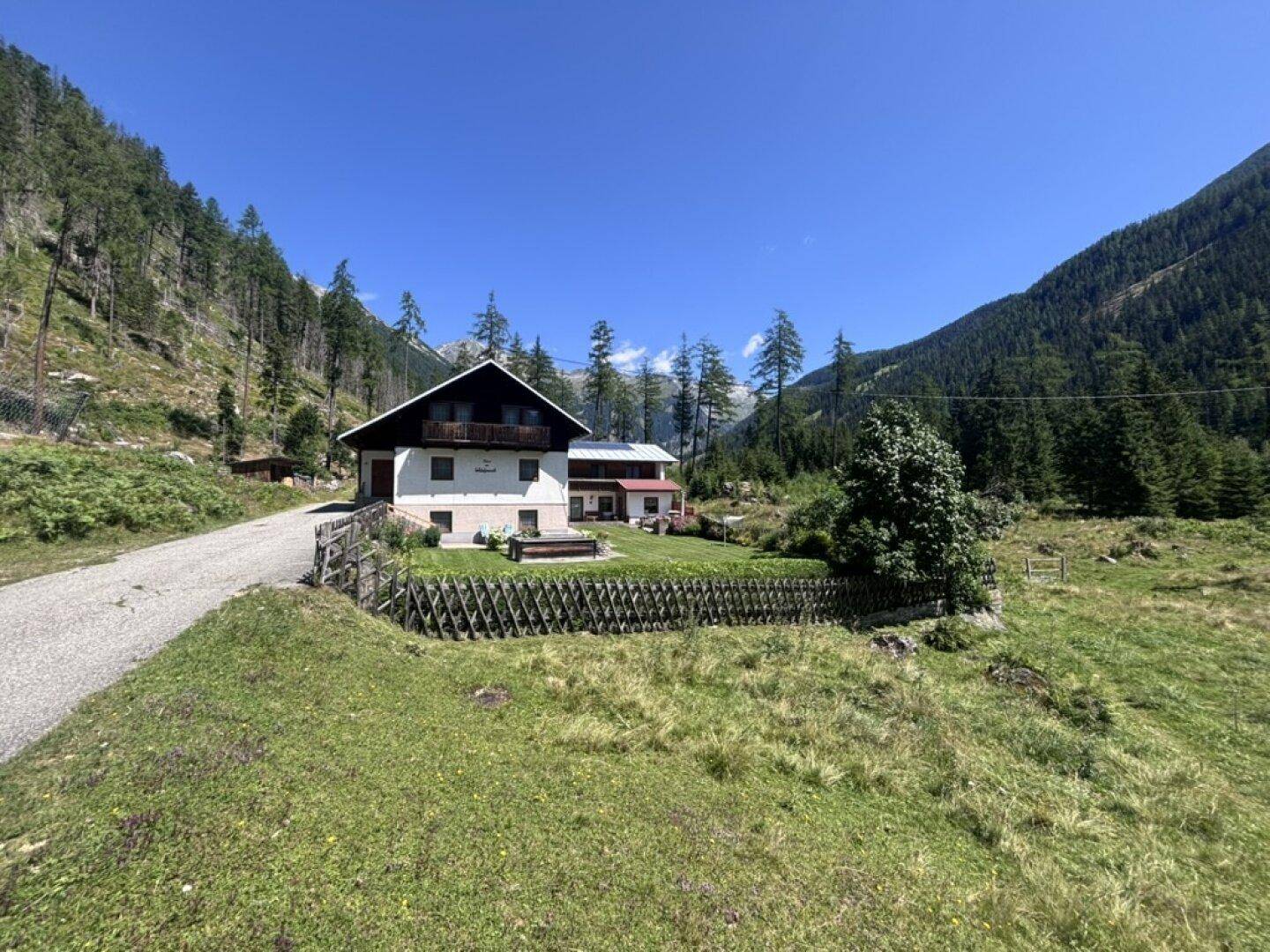 Traditionelles Haus in alpiner Landschaft mit weitem Blick auf die umliegenden Berge und Wälder.