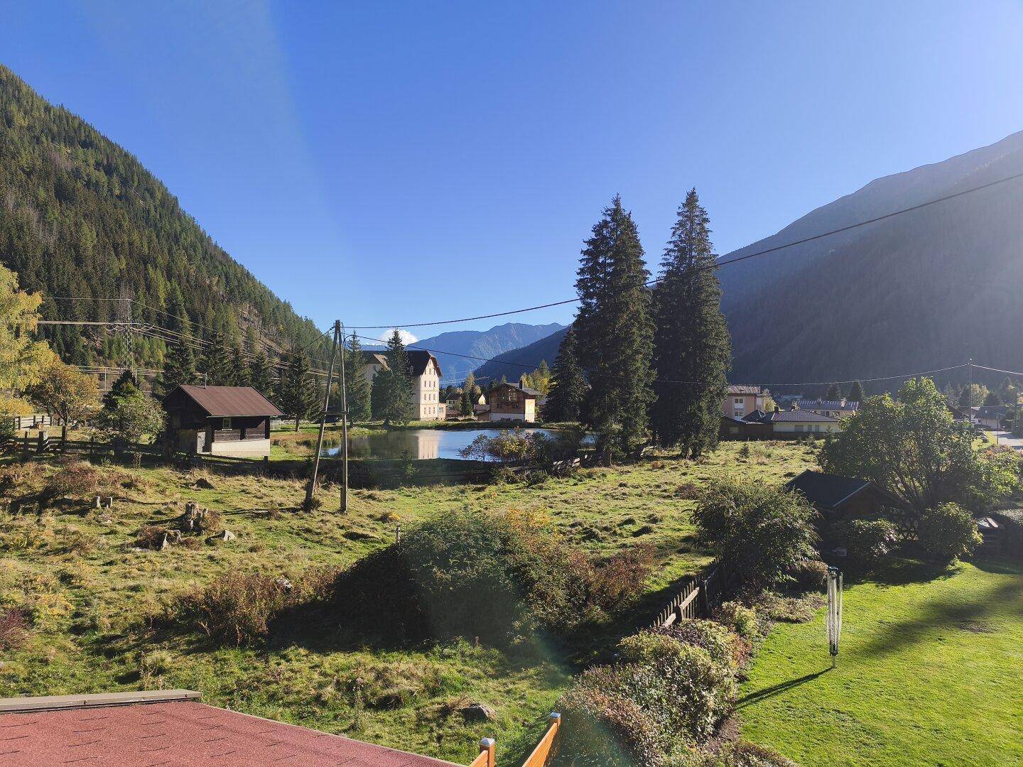 Panoramablick über ein Tal mit einem kleinen See, umgeben von Bergen und ländlicher Bebauung.