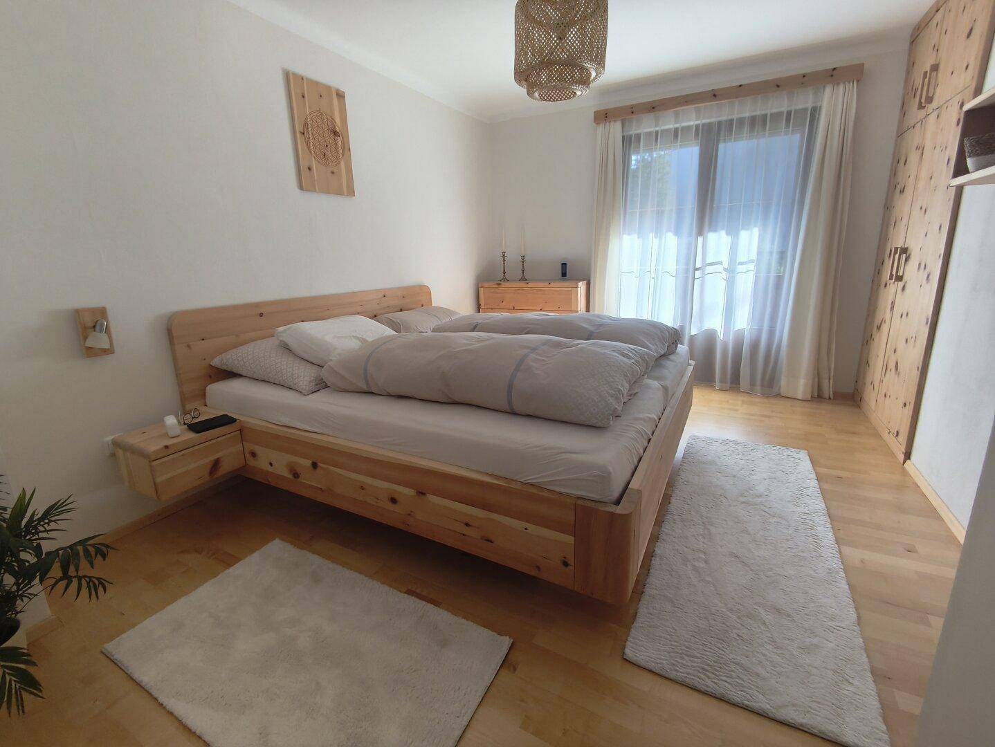Helles Schlafzimmer mit einem Holzbett, passendem Kleiderschrank und Fenster mit Vorhängen.