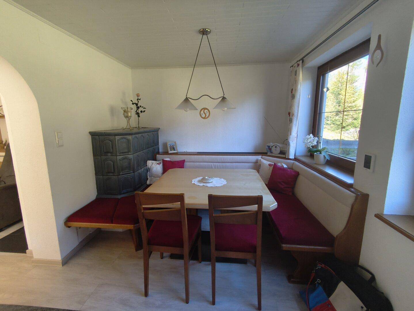 Gemütlicher Essbereich mit Eckbank, Holztisch und einem traditionellen Kachelofen.
