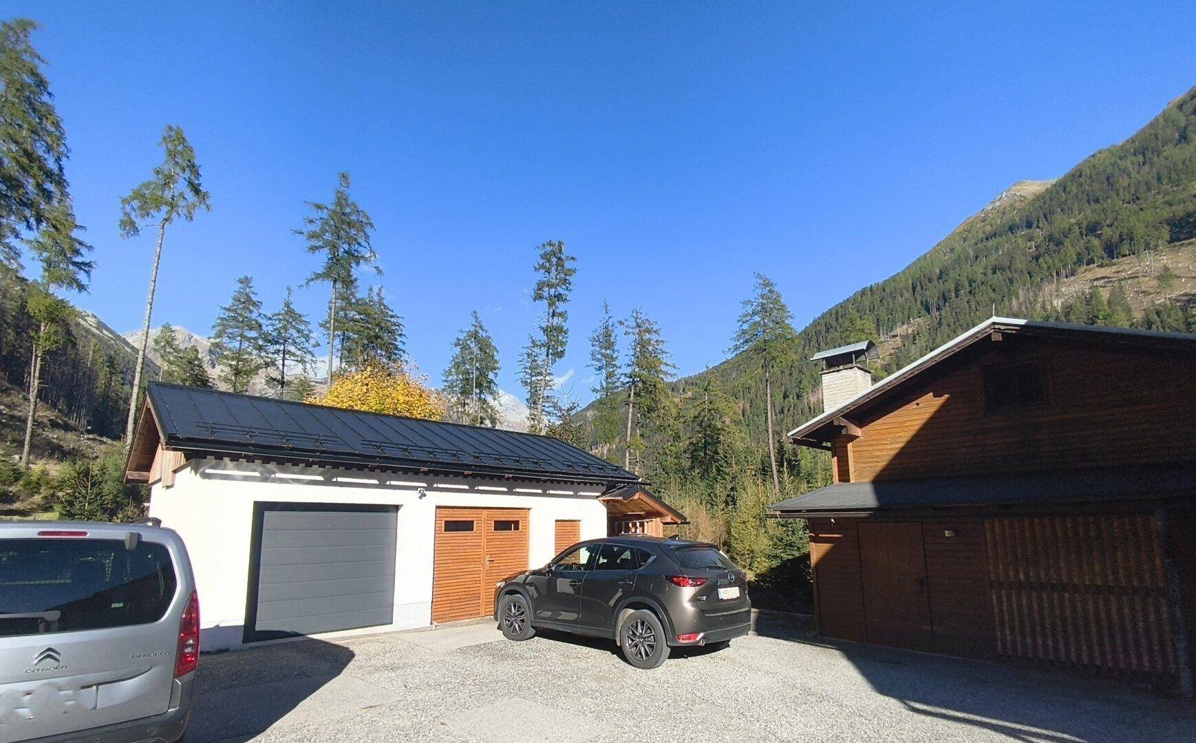 Außenansicht einer Garage und eines Holzgebäudes mit Parkplätzen und Bergblick.