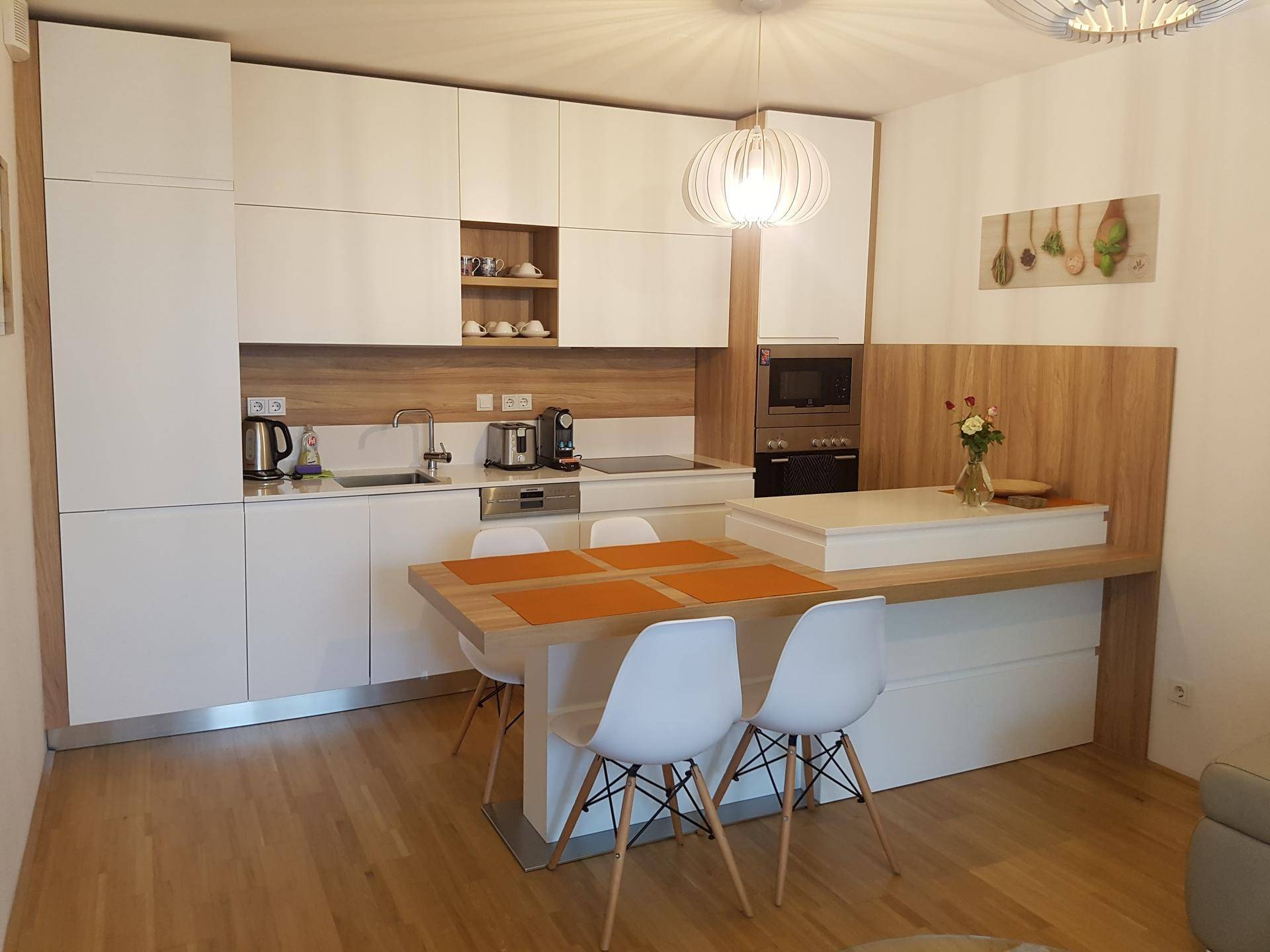 Moderne Einbauküche mit weißen Fronten, Holzakzenten und integriertem Essbereich.