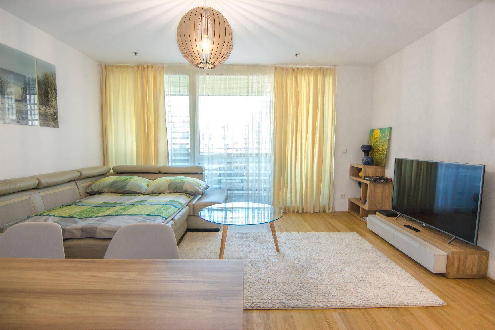 Helles Wohnzimmer mit beigem Sofa, Holzboden und Zugang zu einem Balkon oder einer Terrasse.