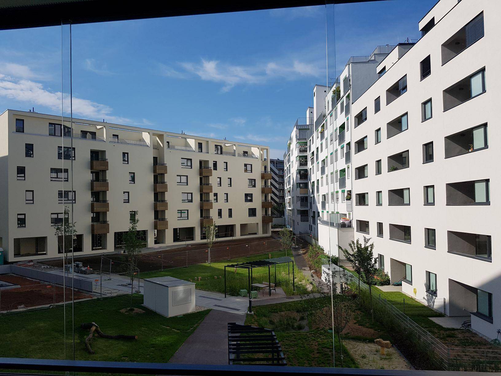 Blick auf einen begrünten Innenhof, umgeben von modernen Wohngebäuden mit Balkonen.