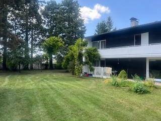 Weitläufiger Gartenbereich hinter dem Haus mit gepflegtem Rasen und hohen Bäumen unter blauem Himmel.