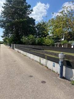Gepflasterter Weg entlang einer niedrigen Mauer mit einem Zaun, umgeben von Bäumen und Grün.
